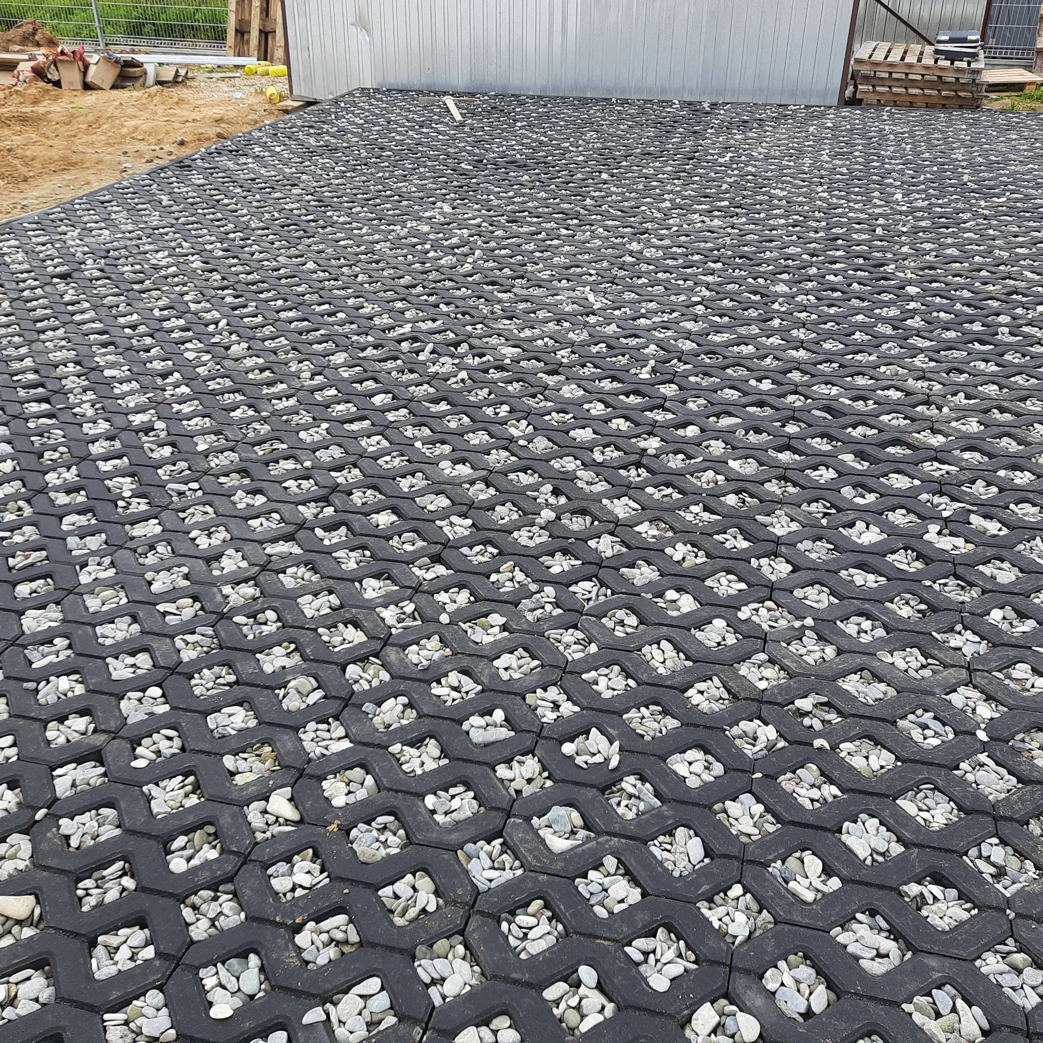 Wykończona nawierzchnia z ażurowych płyt betonowych wypełnionych drobnymi, jasnymi kamieniami na posesji.