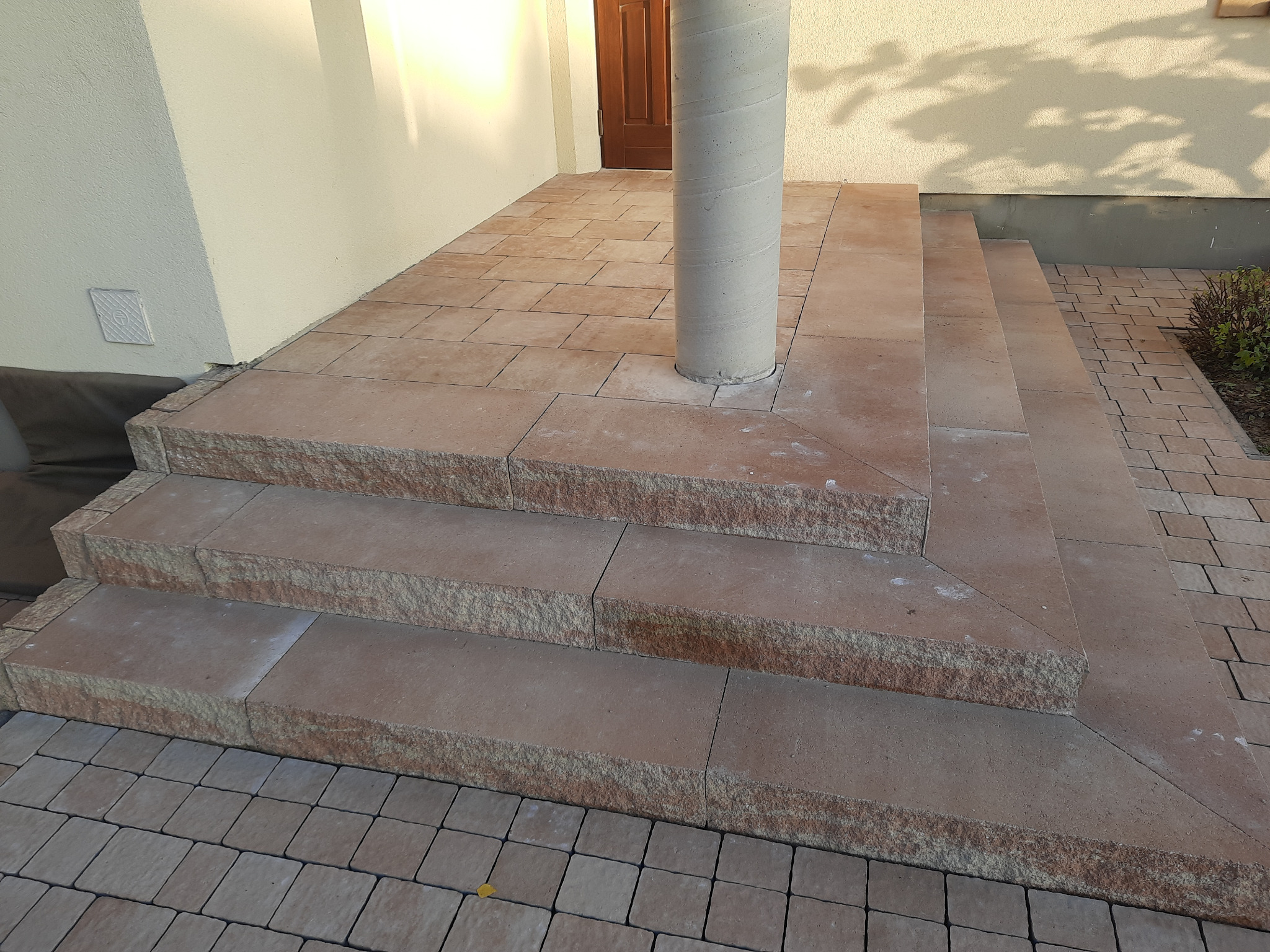 Kamienne schody wejściowe z kolumną, wykonane z kostki brukowej w odcieniach beżu i brązu, prowadzące do drzwi wejściowych.