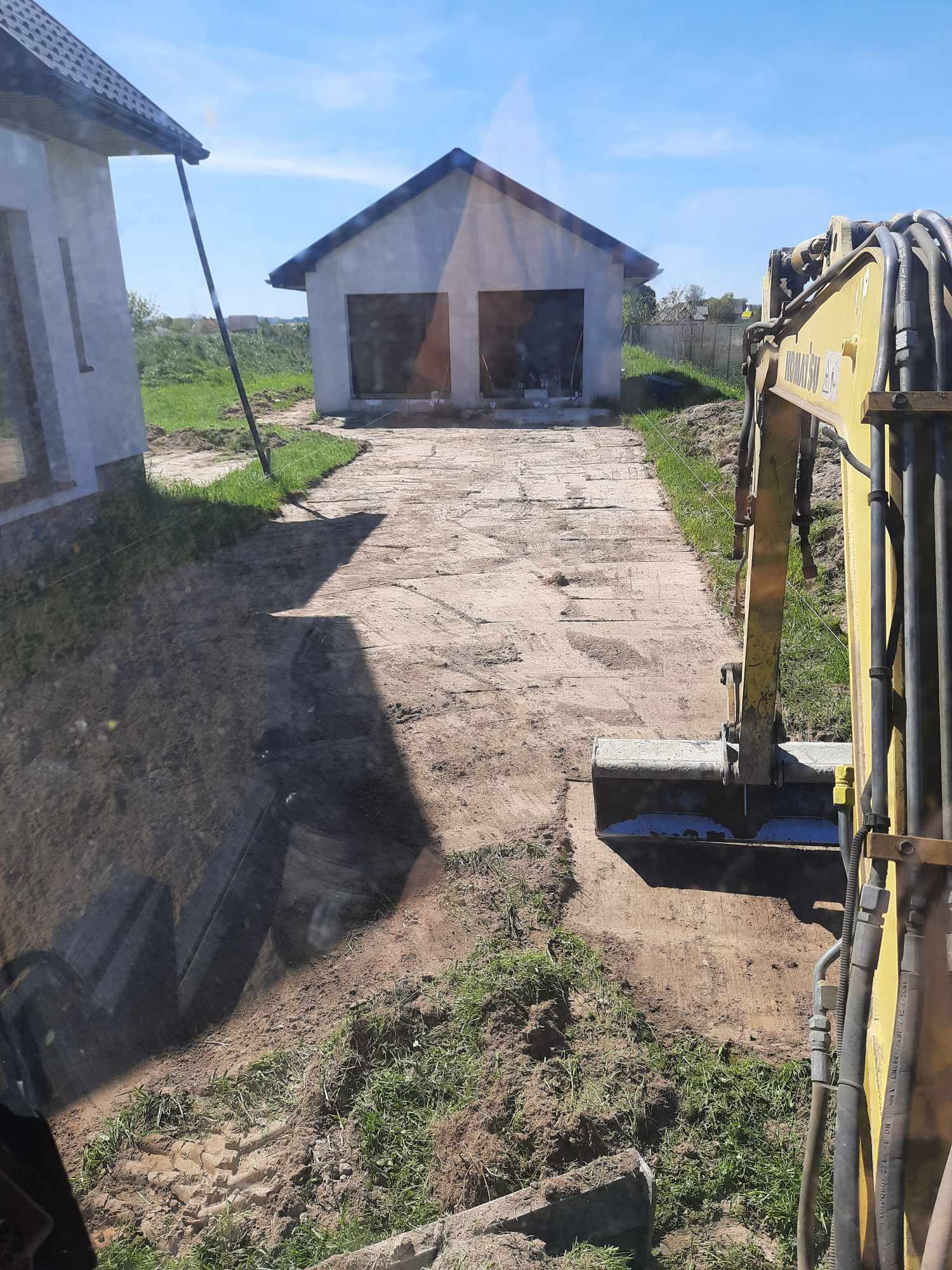Przygotowanie podłoża pod kostkę brukową: żółta koparka Komatsu usuwa ziemię na długim podjeździe do garażu, widok z kabiny operatora.