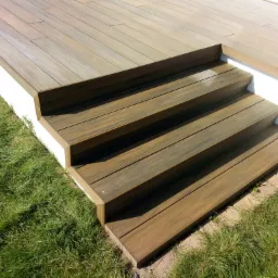 Schody z desek kompozytowych prowadzące na taras, widoczne zielone trawniki po bokach.