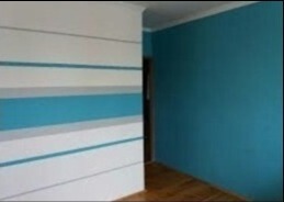 Wnętrze pokoju z pomalowanymi ścianami: jedna ściana w poziome pasy biało-szaro-turkusowe, druga ściana w jednolitym turkusowym kolorze, widoczna podłoga z paneli.