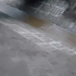 Ujęcie z dołu na betonowy mostek z czerwonymi barierkami, pod którym widać fragment ułożonej kostki brukowej na ziemi.