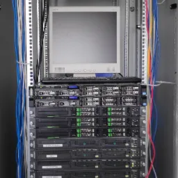 Serwerownia z widocznym monitorem Acer, klawiaturą, przełącznikami sieciowymi i okablowaniem w szafie rack.