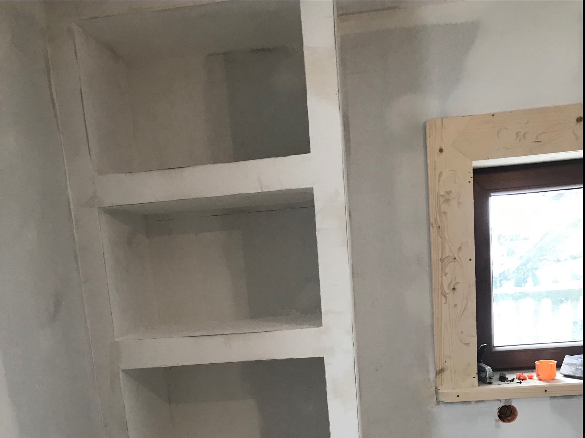 Surowe, niewykończone wnęki ścienne z półkami i ozdobne obramowanie okna w trakcie montażu w Podczerwonym, widoczne ślady po szpachlowaniu i niedoskonałości ścian.
