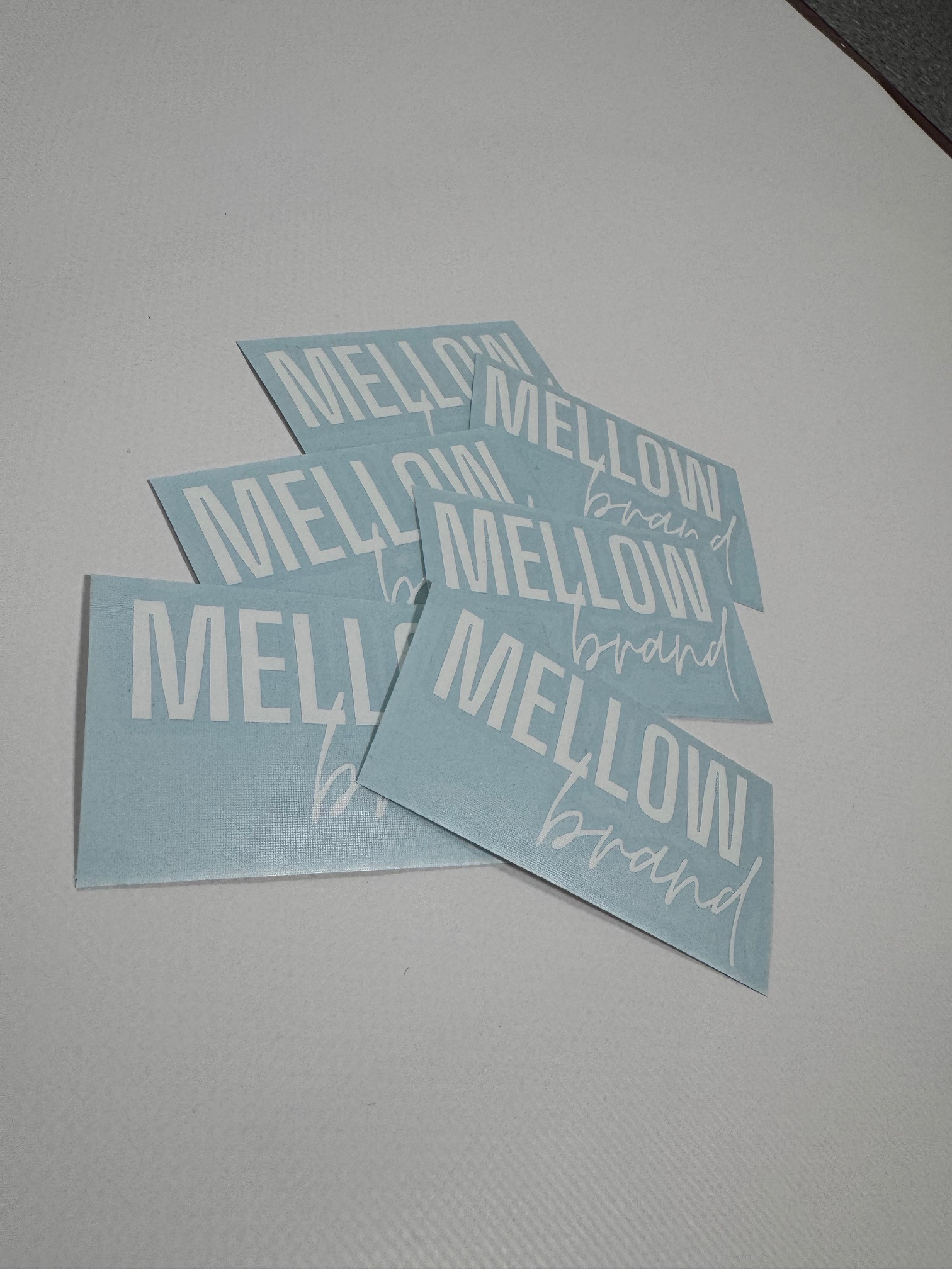 Stos niebieskich, kwadratowych etykiet z białym napisem 'MELLOW brand' leżących na białym tle.