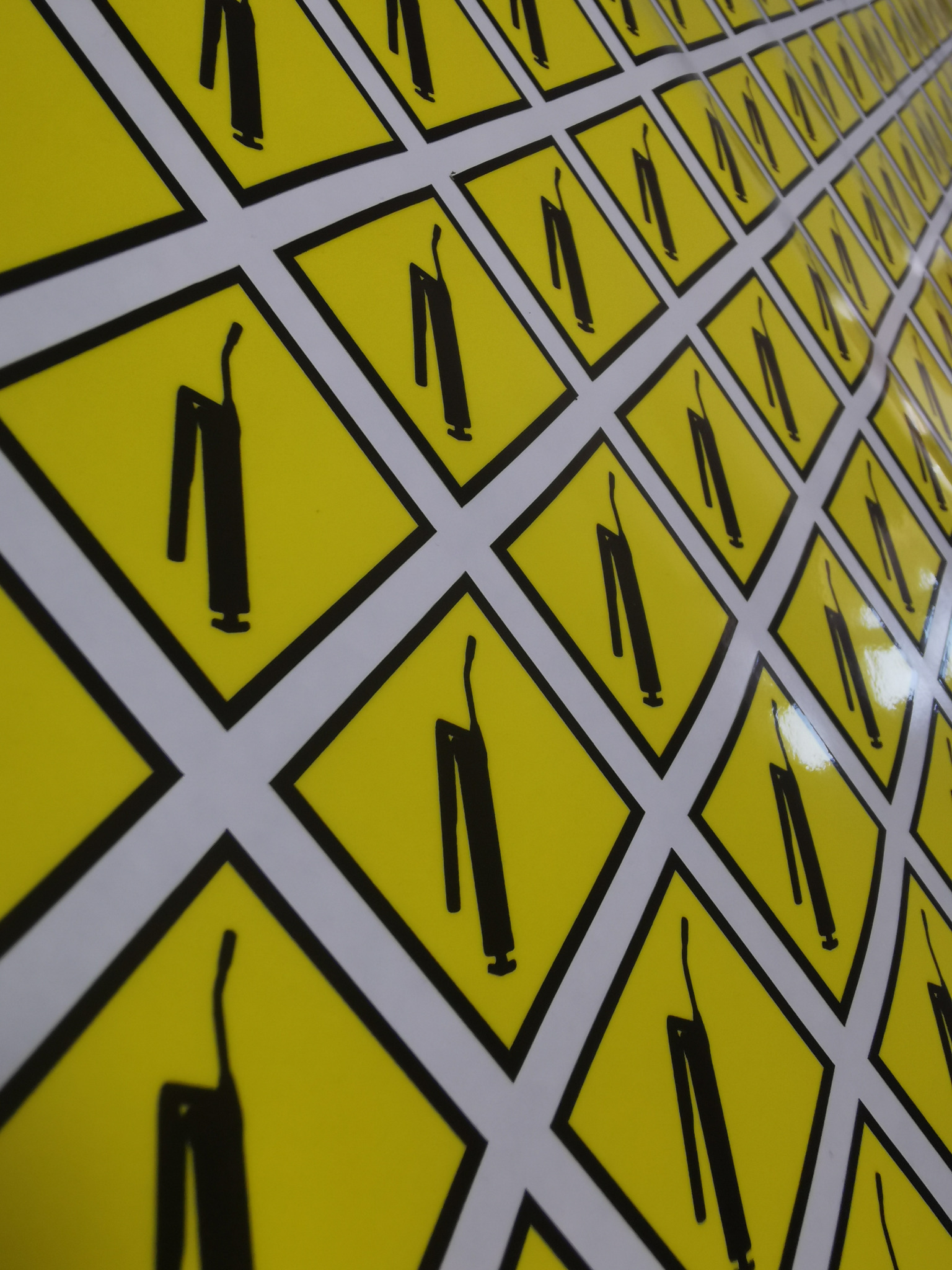 Arkusz z powtarzalnym wzorem czarnych sylwetek pistoletów do kleju na żółtych kwadratach z czarną obwódką, ułożonych na białym tle w regularną siatkę.