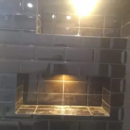 Ciemne, błyszczące płytki ułożone w ścianie z wnękami, oświetlone od góry i od wewnątrz, tworzące minimalistyczny design.