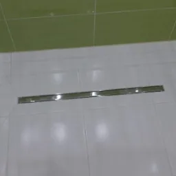 Białe płytki podłogowe z chromowanym odpływem liniowym w kabinie prysznicowej, zielone płytki ścienne.