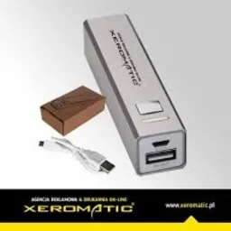 Srebrny powerbank z logo firmy Xeromatic, brązowe pudełko, biały kabel USB na jasnoszarym tle.