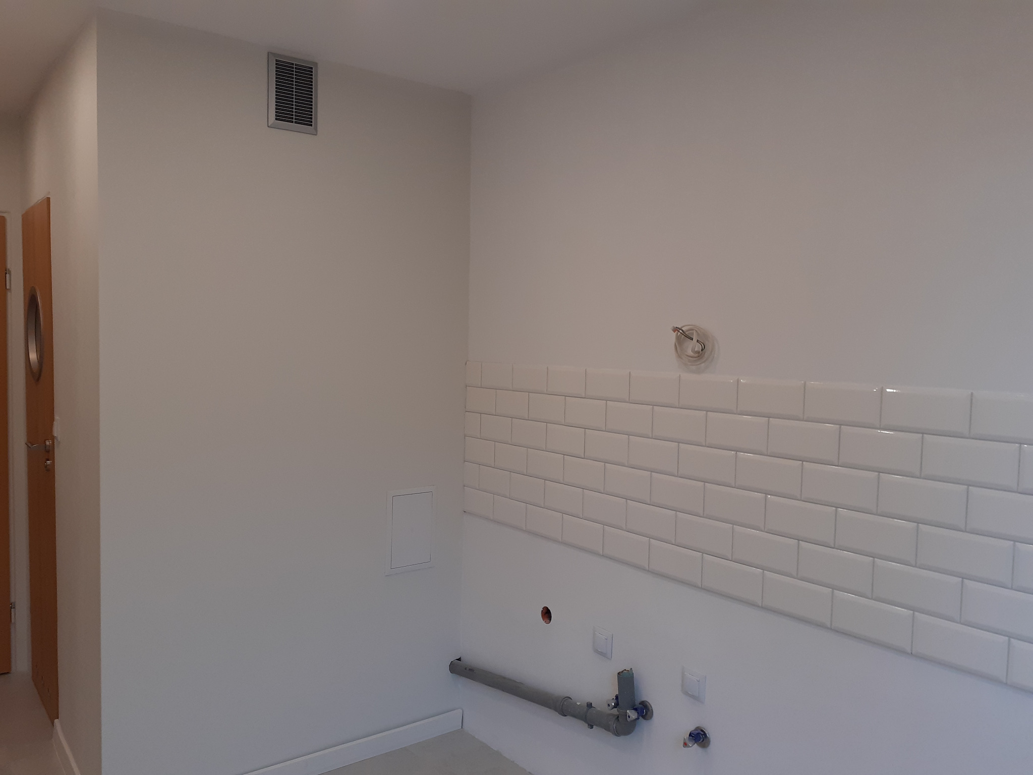 Świeżo ułożone, białe, błyszczące płytki typu metro na ścianie w łazience, widoczne instalacje wodne i elektryczne przed dalszym wykończeniem.