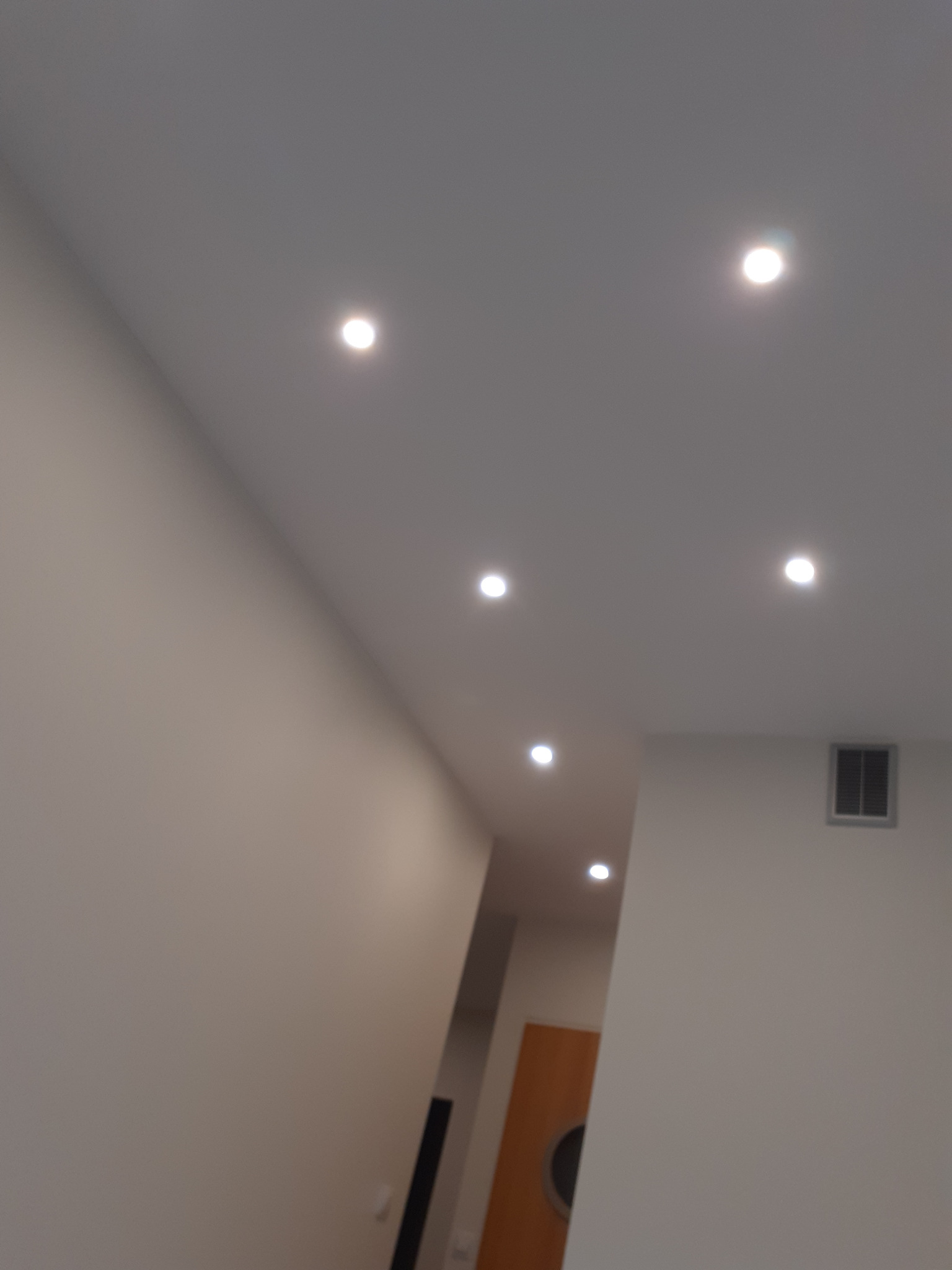 Sufit z zamontowanymi, okrągłymi lampami LED wpuszczanymi, widoczny fragment ściany i drzwi w tle.