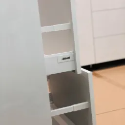 Wysuwane, białe szuflady kuchenne z systemem Blum, widoczne półki i fronty w minimalistycznym stylu.