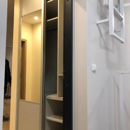 Dece - Meble - Wnętrze przedpokoju z szafą przesuwną, częściowo z lustrem, odsłaniającą półki wewnątrz, obok biała ściana z dekoracyjną, metalową konstrukcją.