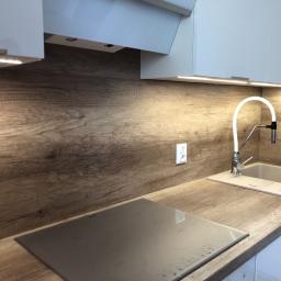 Dece - Meble - Nowoczesna kuchnia z drewnianym blatem, szarym zlewem i płytą indukcyjną; oświetlenie LED pod szafkami górnymi.