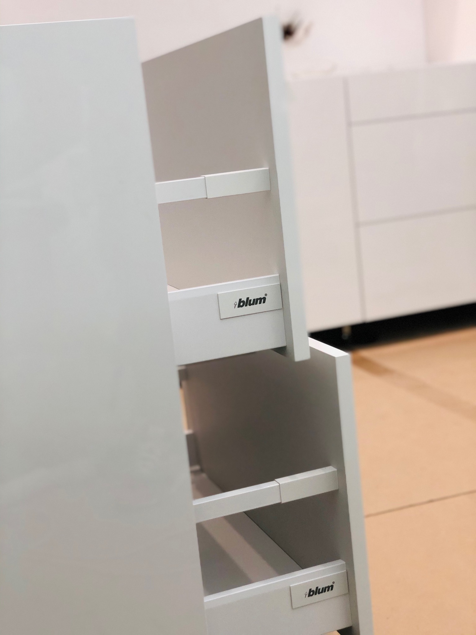 Wysuwane, białe szuflady kuchenne z systemem Blum, widoczne półki i fronty w minimalistycznym stylu.