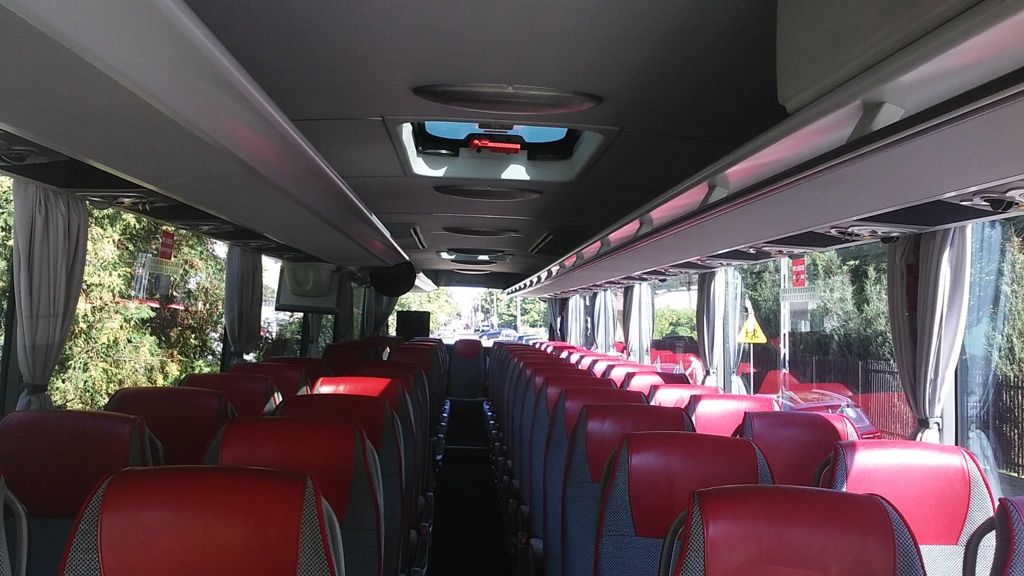 Wnętrze autobusu turystycznego z czerwonymi fotelami i szarymi zasłonami w oknach, widok z przodu pojazdu na puste siedzenia.