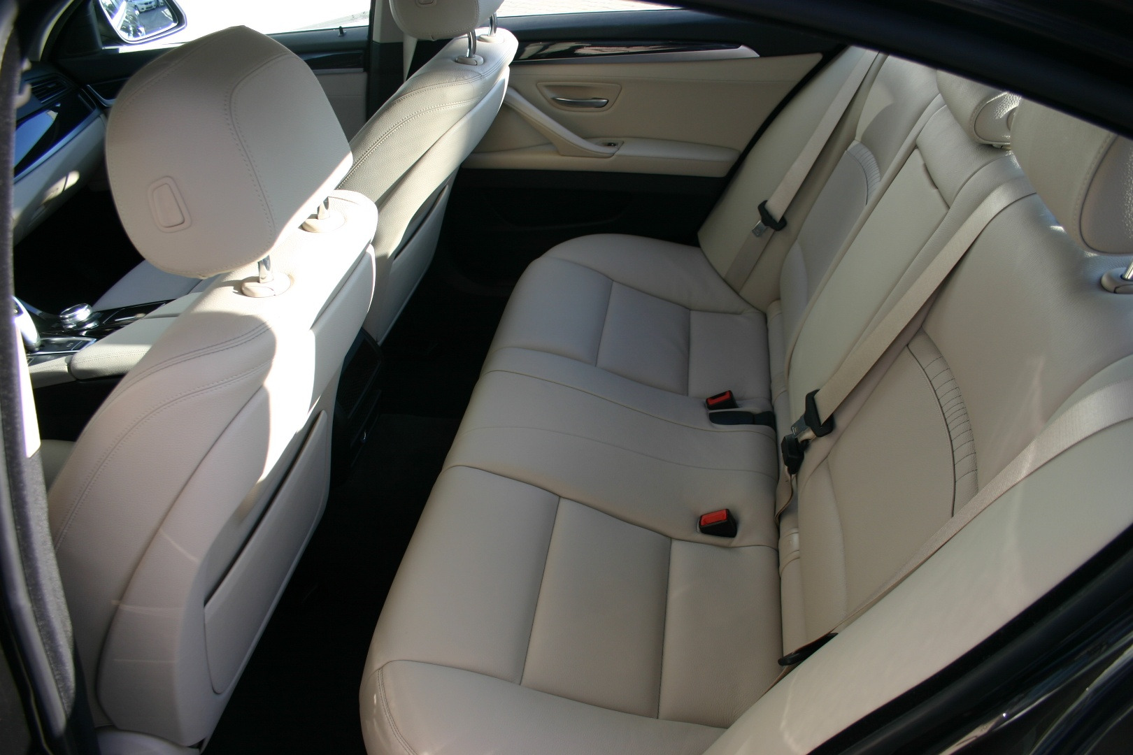 Wnętrze luksusowego samochodu z jasnymi skórzanymi siedzeniami, widoczne pasy bezpieczeństwa i zagłówki.