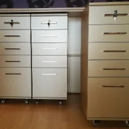 Zestaw mobilnych szafek z szufladami, niektóre zamykane na klucz, na kółkach, z metalowymi uchwytami, na drewnianej podłodze.