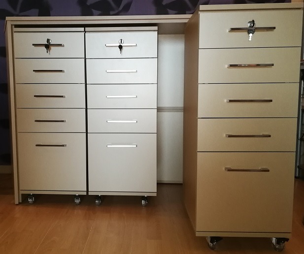 Zestaw mobilnych szafek z szufladami, niektóre zamykane na klucz, na kółkach, z metalowymi uchwytami, na drewnianej podłodze.