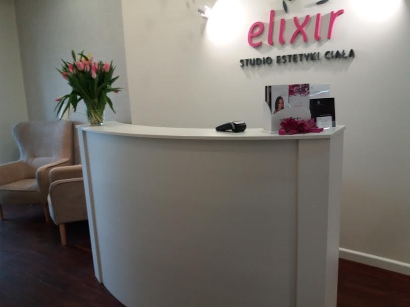 Recepcja w salonie urody z białym, zaokrąglonym blatem, bukietem tulipanów i fotelem w tle.