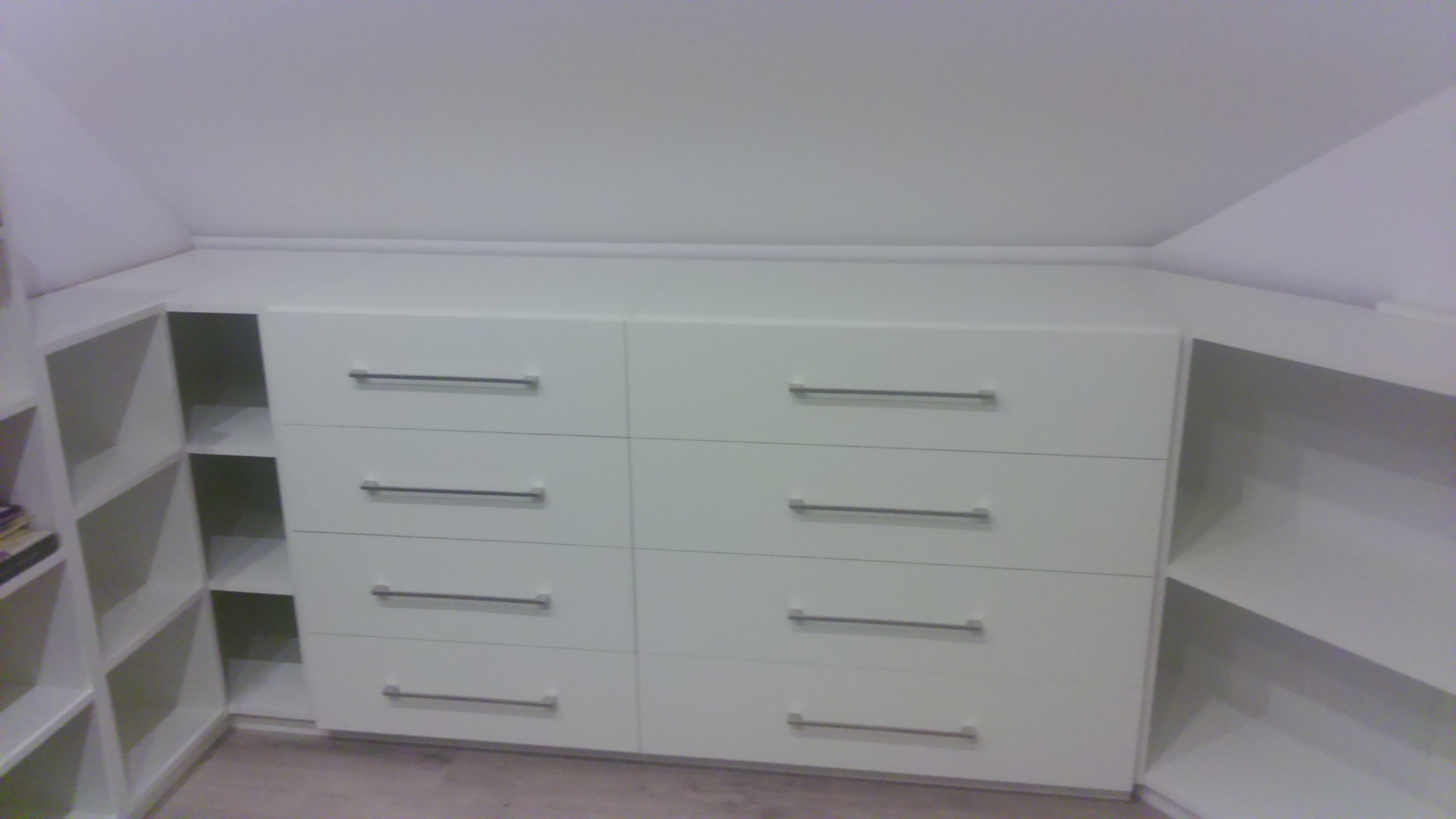 Biała szafa na wymiar z sześcioma szufladami i otwartymi półkami, dopasowana do skosu dachu.