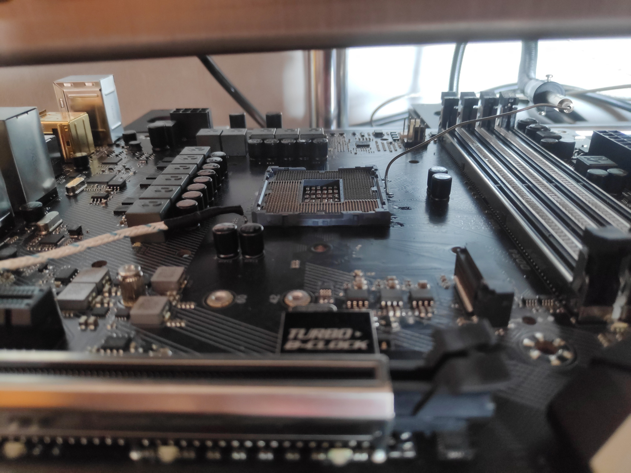 Czarna płyta główna z widocznym gniazdem procesora, slotami pamięci RAM oraz elementami elektronicznymi; ujęcie z bliska, lekko rozmyte.