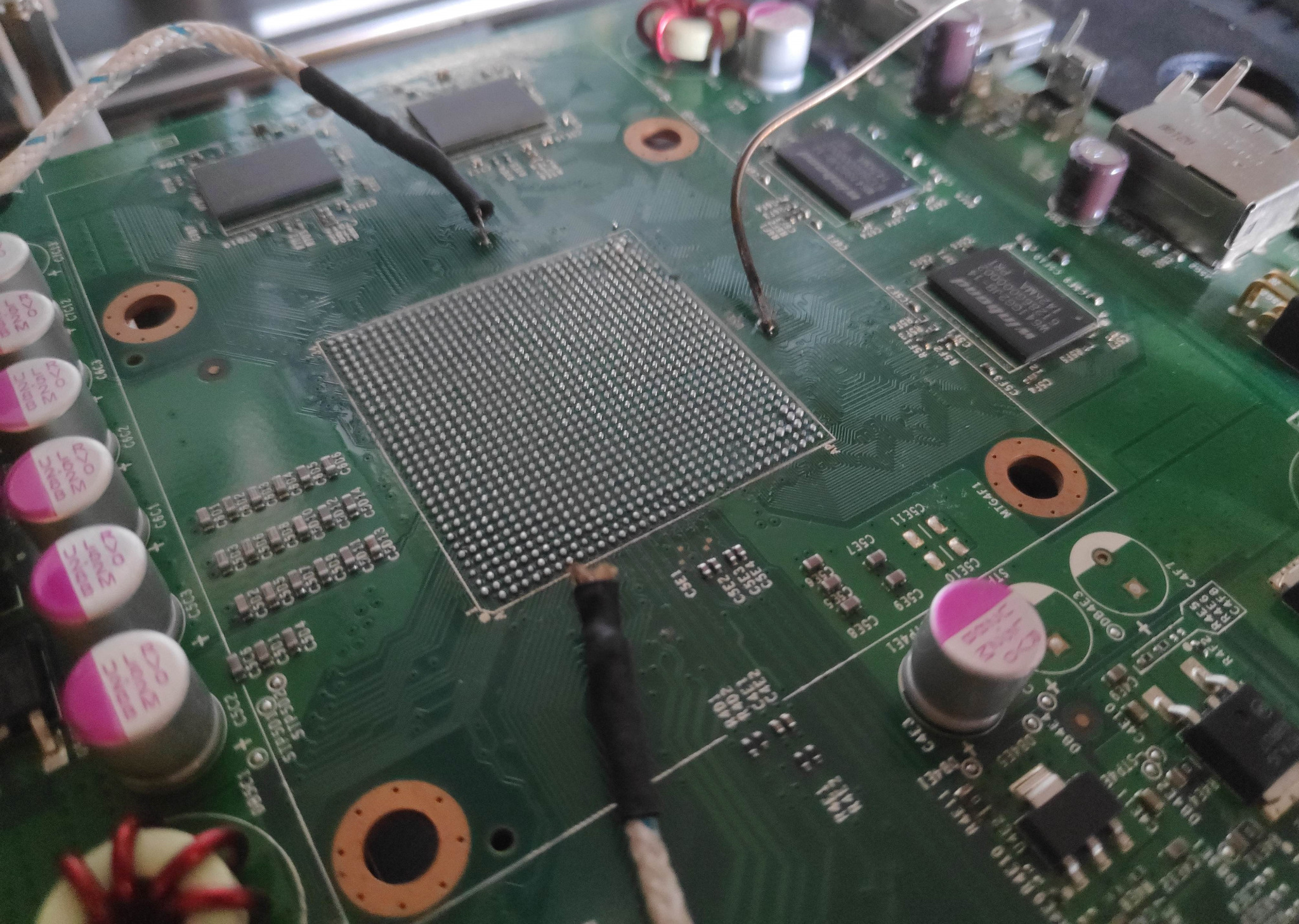 Zielona płyta główna komputera z widocznym układem BGA, elementami elektronicznymi i przewodami, sfotografowana z bliska podczas potencjalnej naprawy w Międzychodzie.