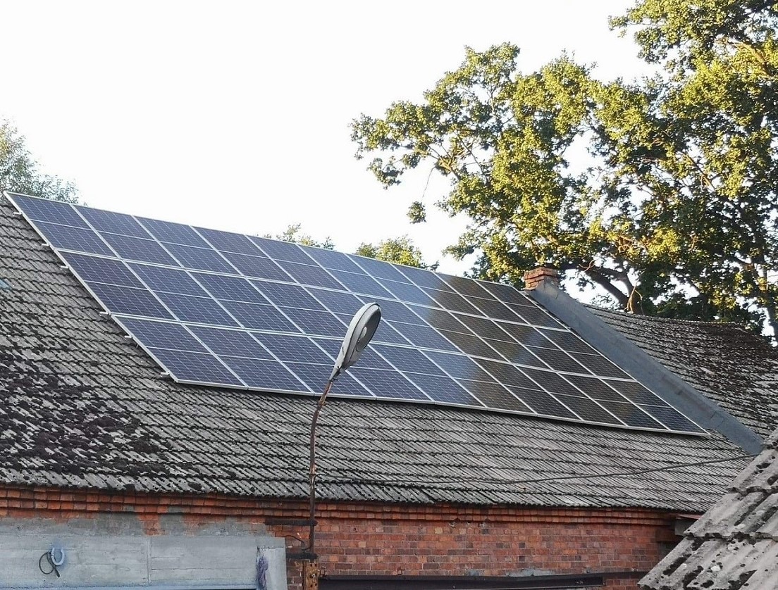 Panel słoneczny na dachu starego ceglanego budynku z kominem i latarnią uliczną z przodu.