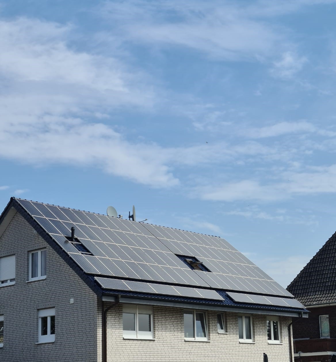 Dom z jasnej cegły z panelami słonecznymi na dachu pod błękitnym niebem z chmurami.