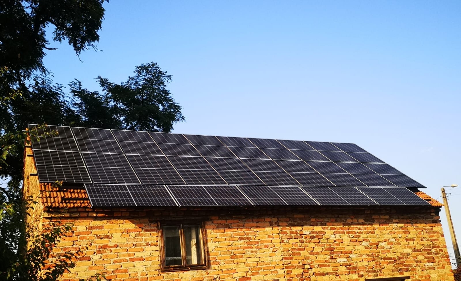 Panele fotowoltaiczne na dachu starego ceglanego domu, widok z dołu w słoneczny dzień.
