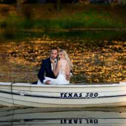 Para młoda w łódce Texas 380 na jeziorze z opadłymi liśćmi, on w granatowym garniturze, ona w białej sukni z koronkowymi plecami, jesienna sceneria