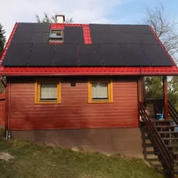 Czerwony dom jednorodzinny z panelami słonecznymi na dachu w Jarosławiu. Widoczne okna z żółtymi ramami i schody wejściowe.