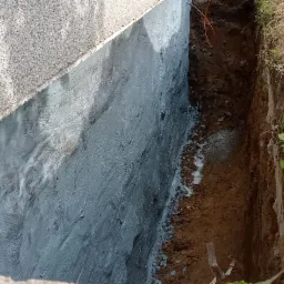 Świeżo zaizolowany fundament budynku, widoczny wykop z ziemią i wystające kable.