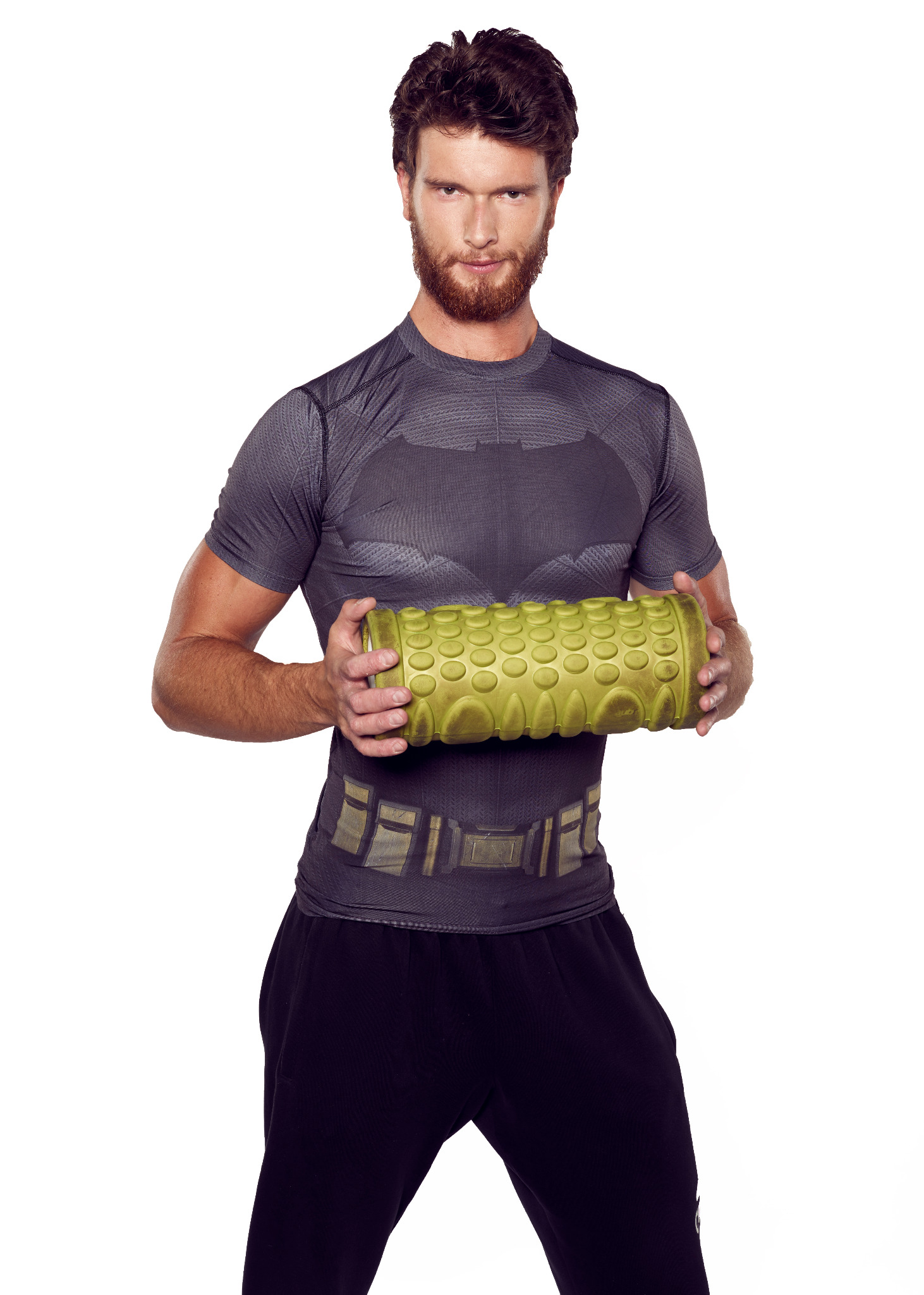 Mężczyzna w koszulce z motywem Batmana trzymający zielony roller do masażu na białym tle.