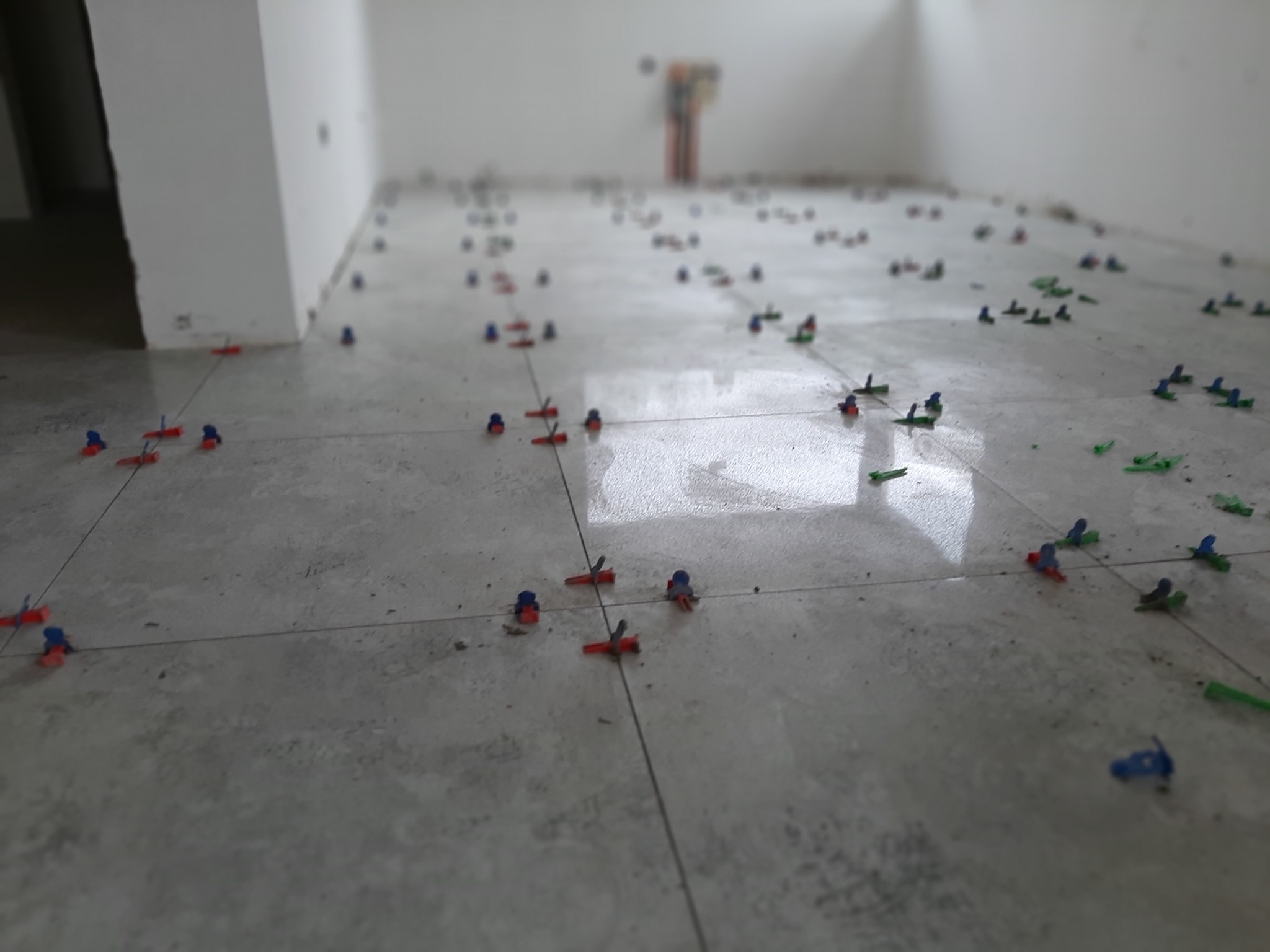 Układanie płytek podłogowych w Lublinie, z użyciem klipsów poziomujących w kolorach czerwonym, niebieskim i zielonym, widoczne fugi i pozostałości kleju.