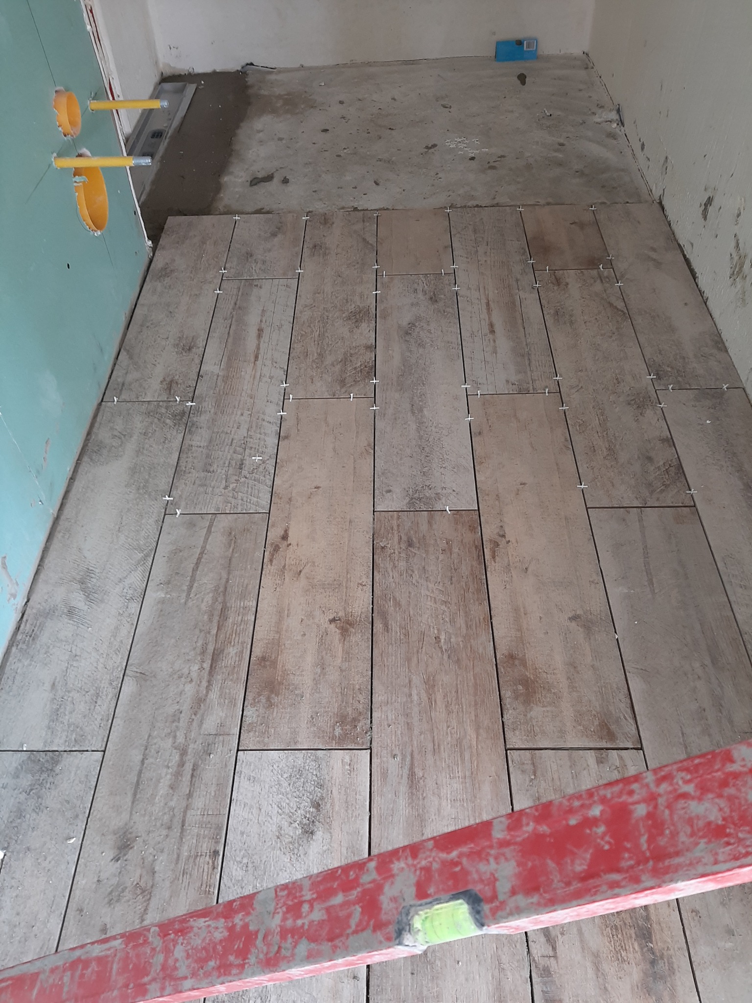 Układanie podłogi z płytek imitujących drewno w łazience, widoczne krzyżyki dystansowe i poziomica