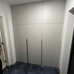 Tabre Sp. z o.o. - Szafa wnękowa z szarymi frontami, czarnymi uchwytami, zamontowana od podłogi do sufitu, widoczne listwy przypodłogowe i fragment podłogi w odcieniach granatu.