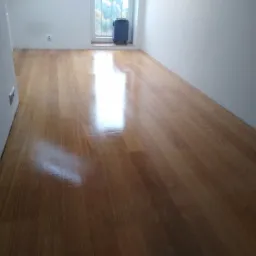 Błyszcząca, świeżo wycyklinowana podłoga drewniana w pustym pokoju z bagażem przy oknie.