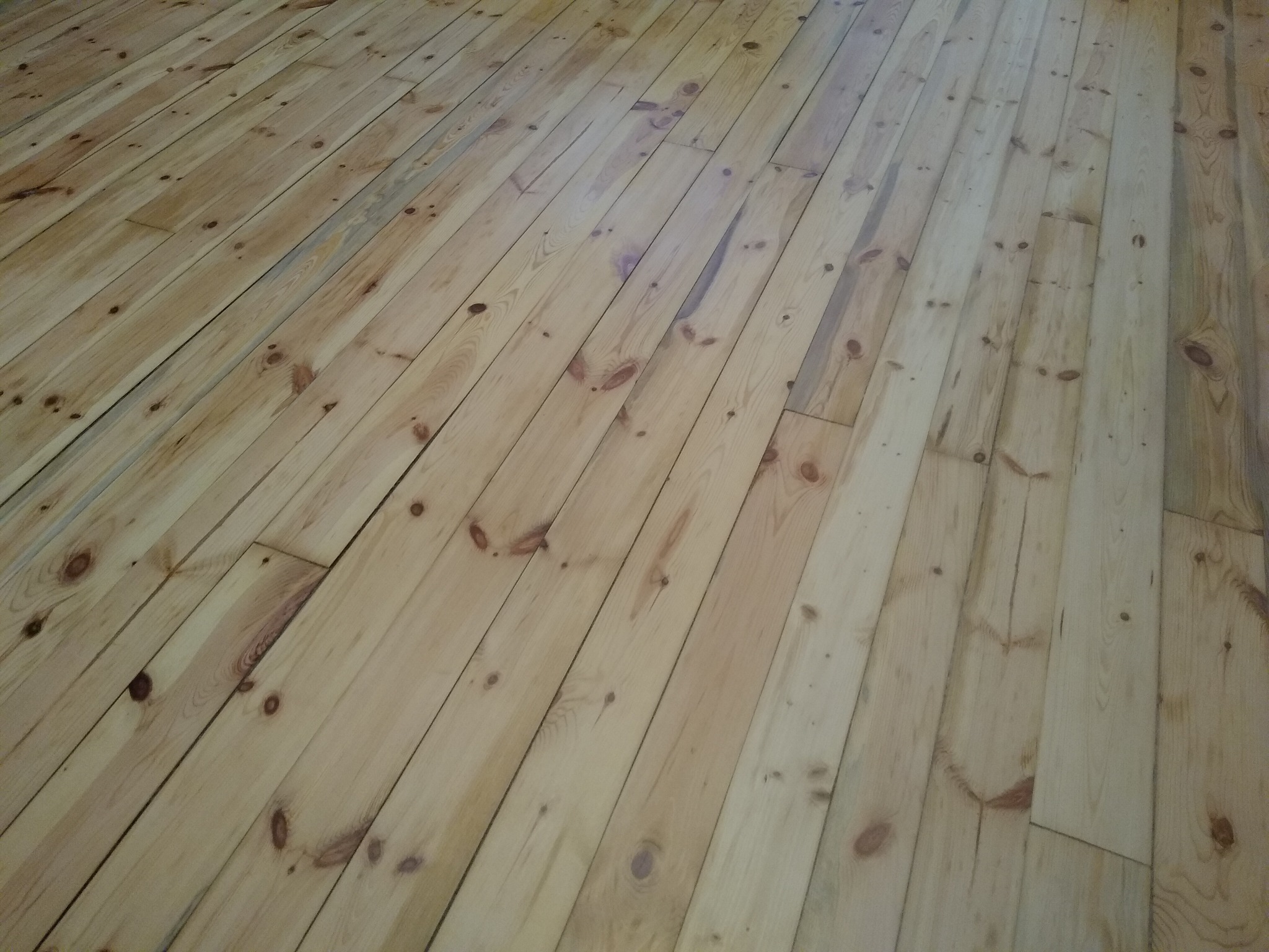 Jasna, drewniana podłoga z widocznymi sękami, ułożona ukośnie, w naturalnym odcieniu drewna.