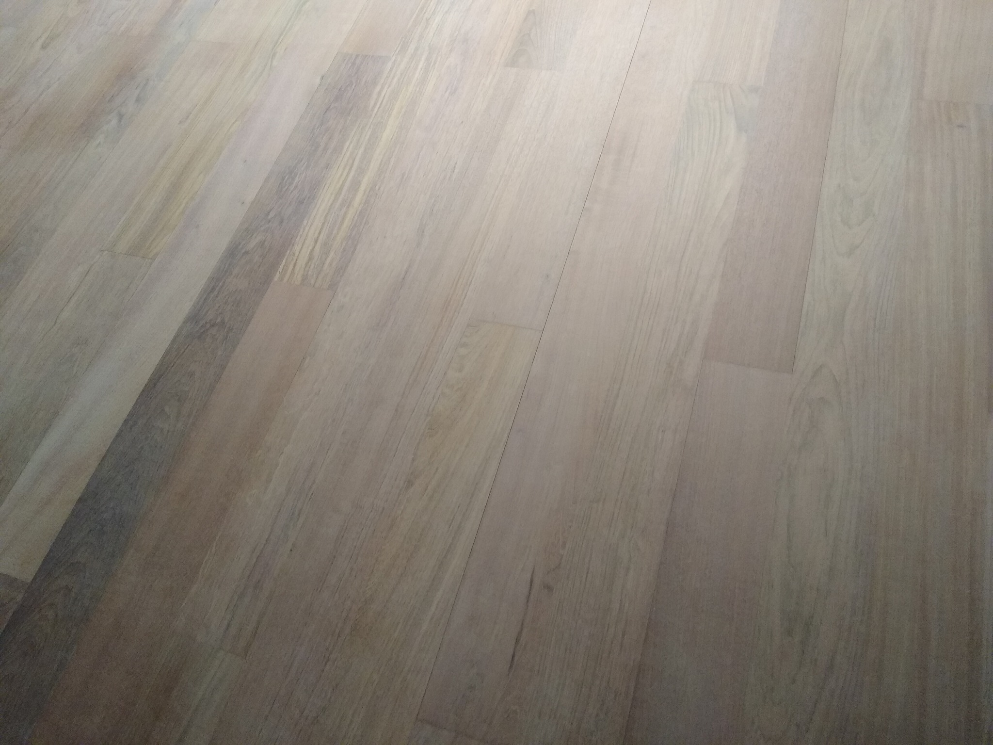 Ułożone panele podłogowe w jasnym odcieniu drewna, widoczne z perspektywy pod kątem, ukazujące strukturę i łączenia paneli.