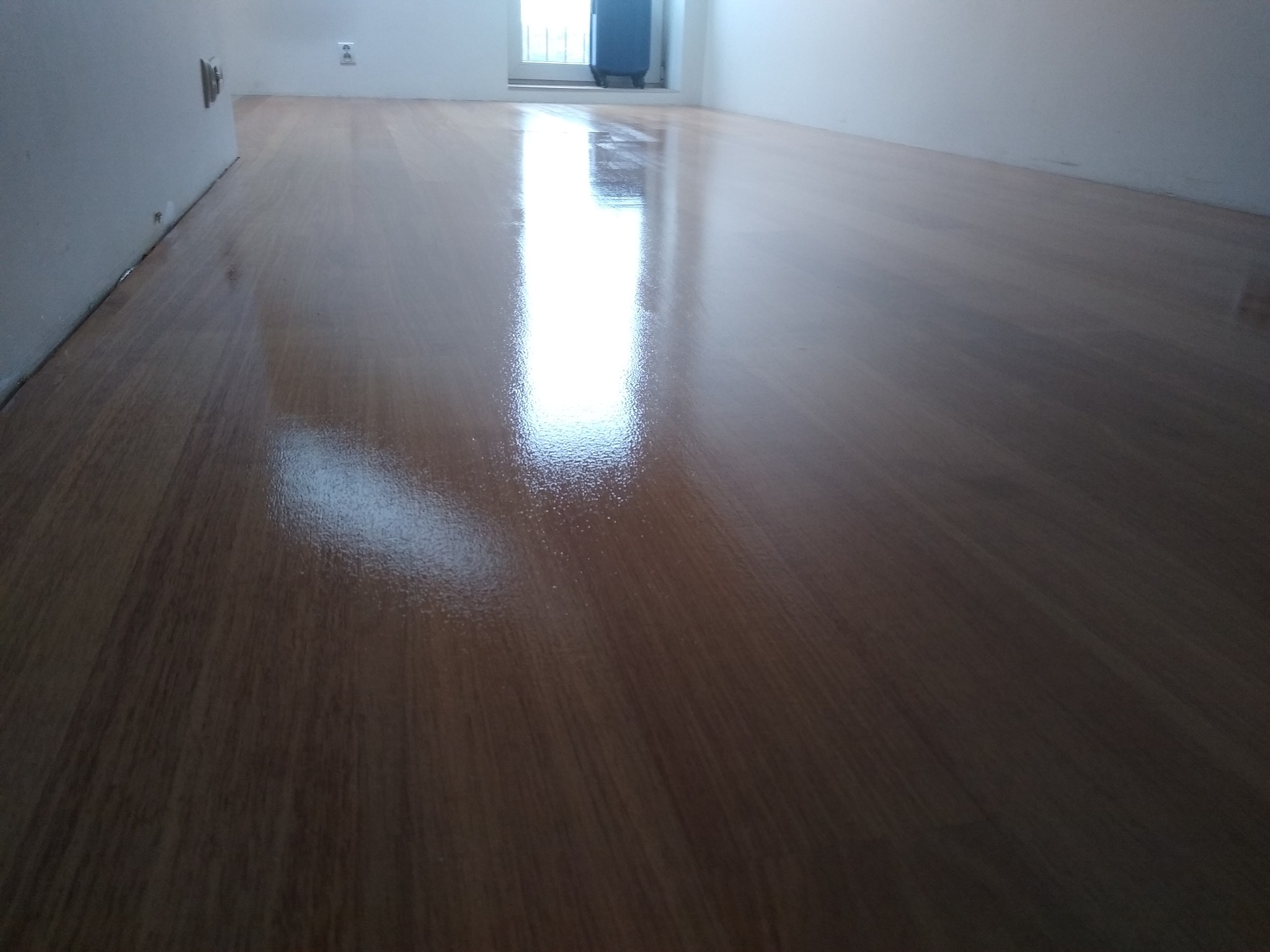 Błyszcząca, świeżo polakierowana podłoga z parkietu w pustym pomieszczeniu, odbijająca światło okna.