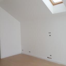 Daniel - Wnętrze poddasza po remoncie: świeżo pomalowane białe ściany, jasna podłoga, okno dachowe i widoczne punkty instalacji elektrycznej.