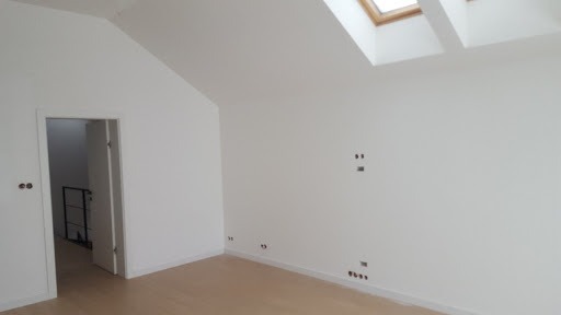 Wnętrze poddasza po remoncie: świeżo pomalowane białe ściany, jasna podłoga, okno dachowe i widoczne punkty instalacji elektrycznej.