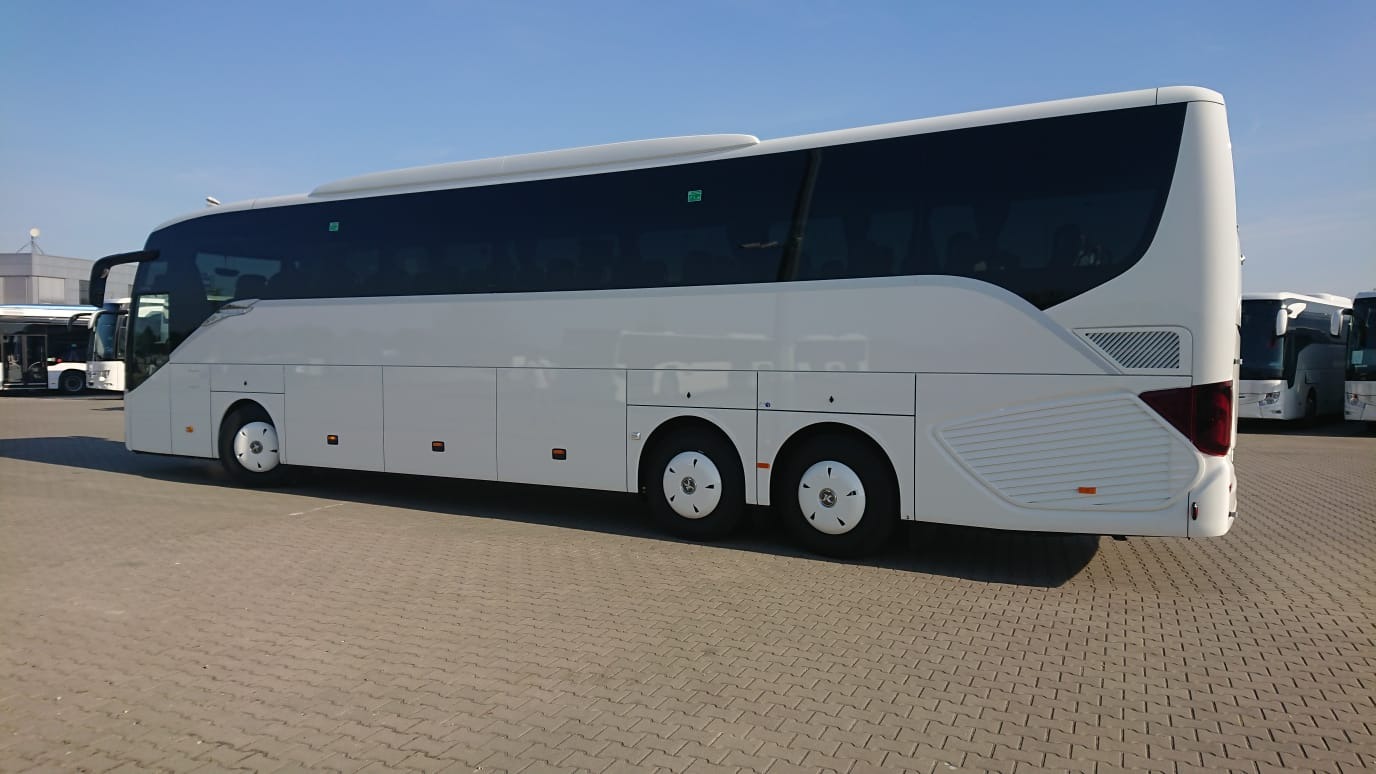 Nowoczesny, biały autokar turystyczny z przyciemnianymi szybami, zaparkowany na placu z kostki brukowej, widok z boku.