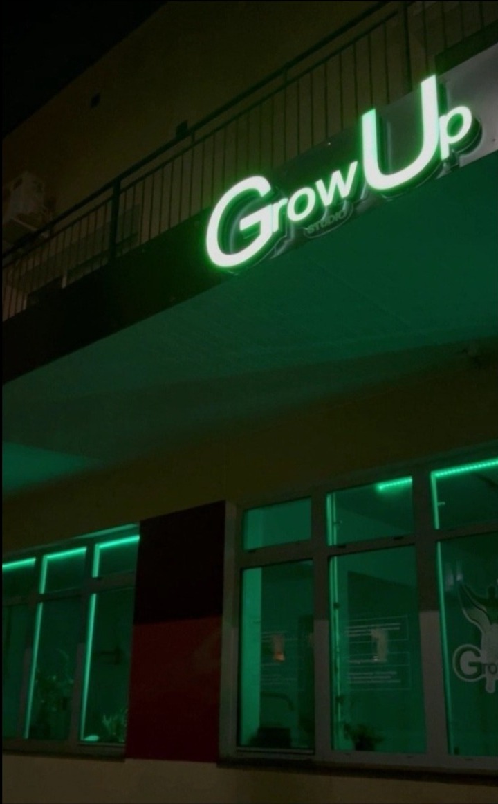 Fasada budynku z neonowym napisem 'Grow Up Studio' w kolorze zielonym, oświetlone okna w tym samym kolorze, balkon z metalową balustradą.