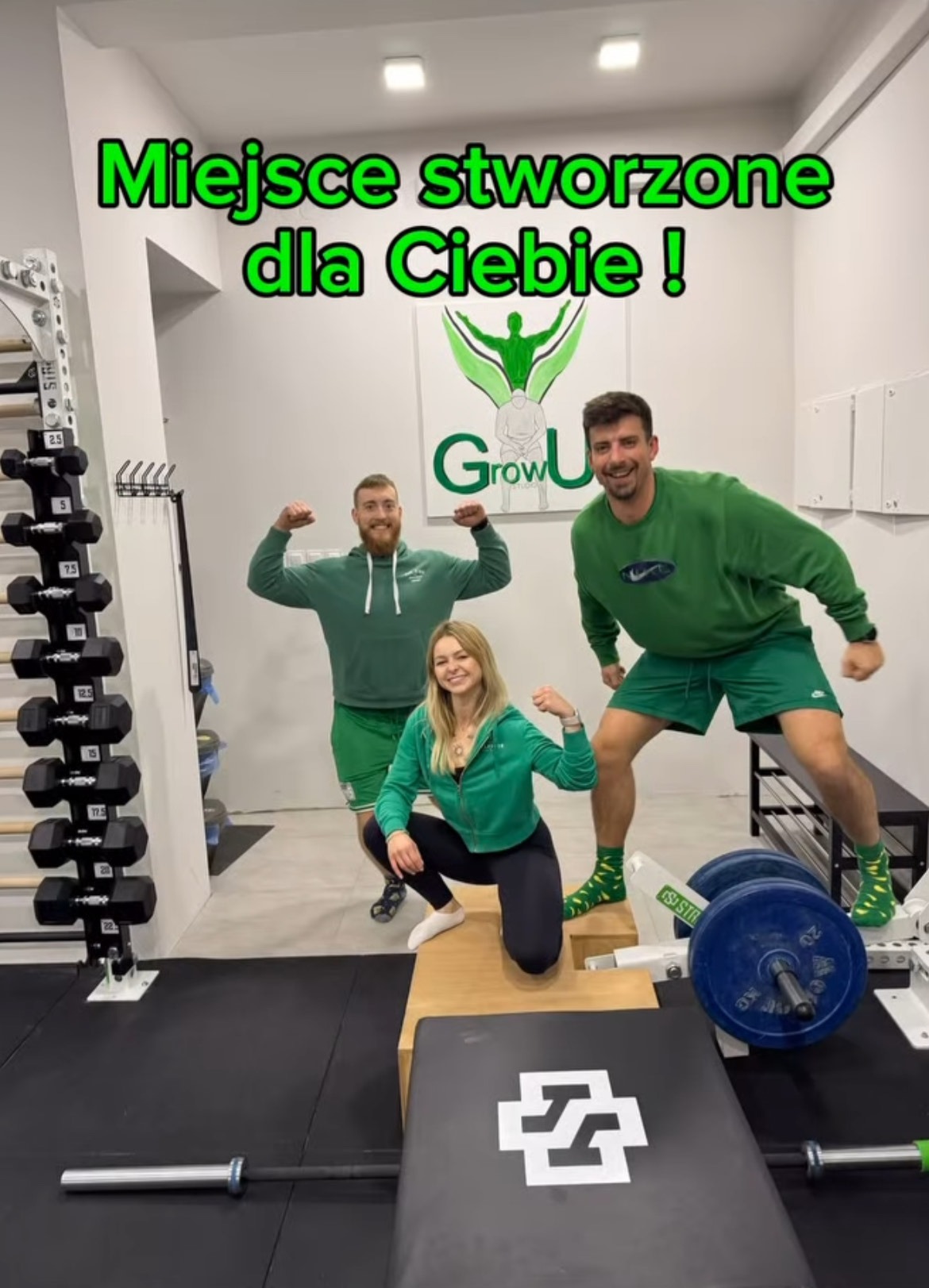 Trzy osoby w zielonych ubraniach pozują w siłowni, prezentując bicepsy; w tle logo Grow Up Studio i stojak z hantlami.