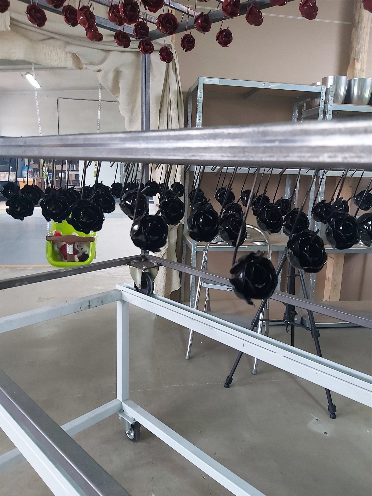 Częstochowa: Metalowe róże, niektóre pomalowane na czarno, inne na czerwono, wiszą na metalowym stojaku w warsztacie, gotowe do dalszej obróbki lub transportu.