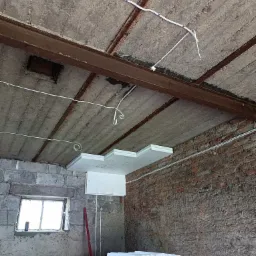 Wnętrze w trakcie prac remontowych: widoczny surowy betonowy sufit z metalowymi belkami, nowa instalacja elektryczna w białych peszlach oraz częściowo zamontowane płyty styropianowe do izolacji...