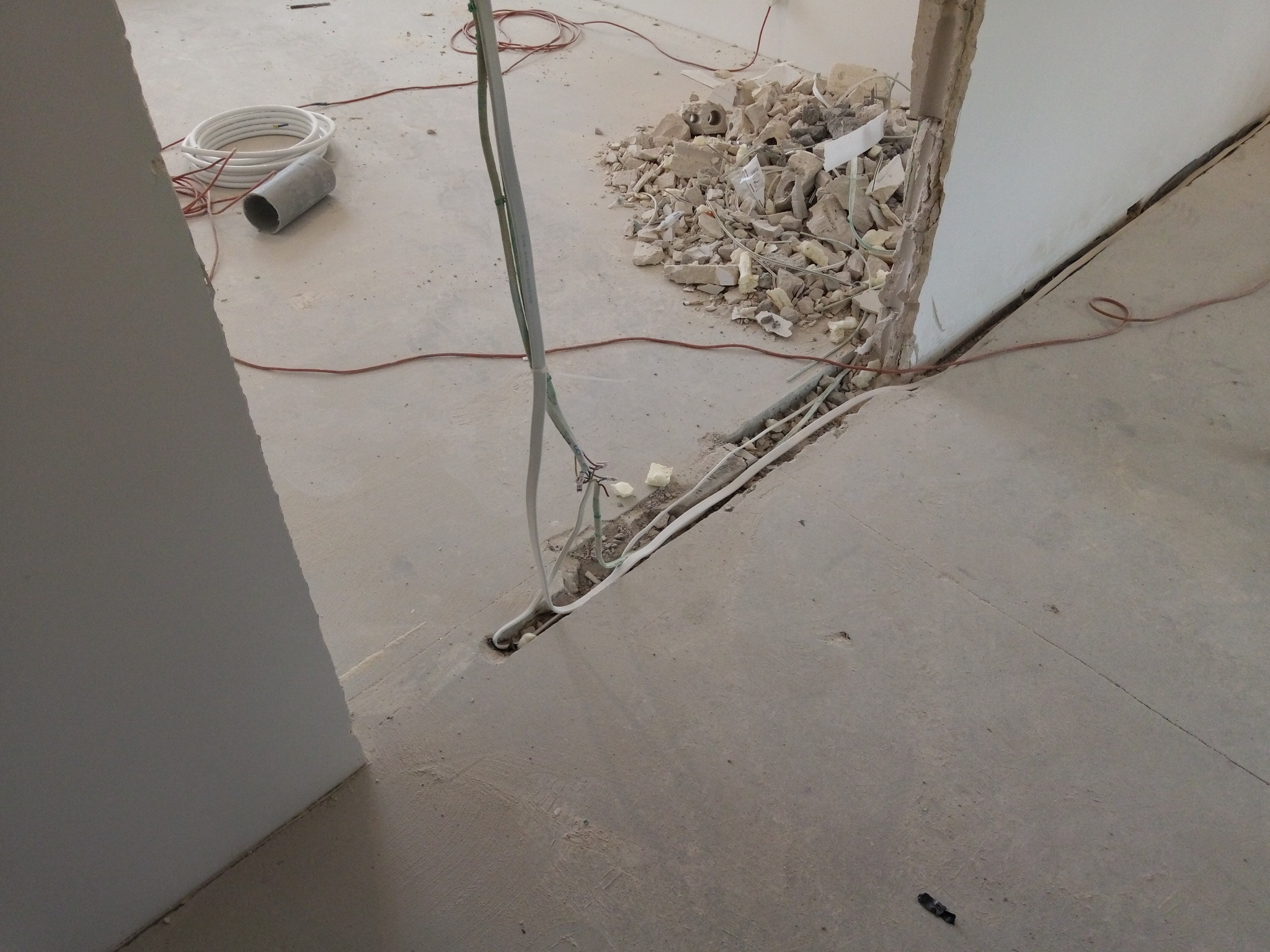 Przygotowanie bruzdy w posadzce pod przewody elektryczne, widoczne kable, rury i gruz po kuciu.