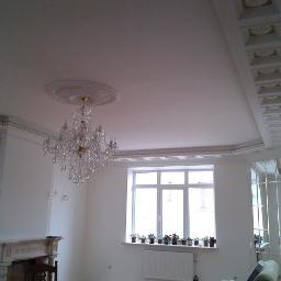 Q - Rem - Jasne wnętrze pokoju po remoncie z ozdobnym sufitem, kryształowym żyrandolem, marmurowym kominkiem i lustrami na ścianie.